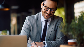 Happy businessman signing paperwork while working on computer in a cafe. Copy space.